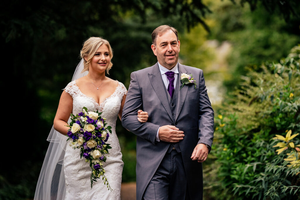 Bride and the man walking her down the aisle on the tree lined path to St James Church, Cheshire wedding photographer