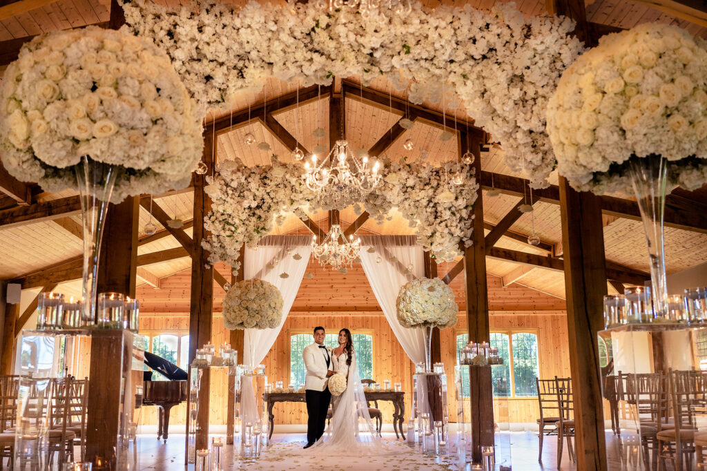 Gemma and Tyrone standing in the Merrydale Manor ceremony room under hanging white flowers and crystal chandeliers, Cheshire wedding photographer