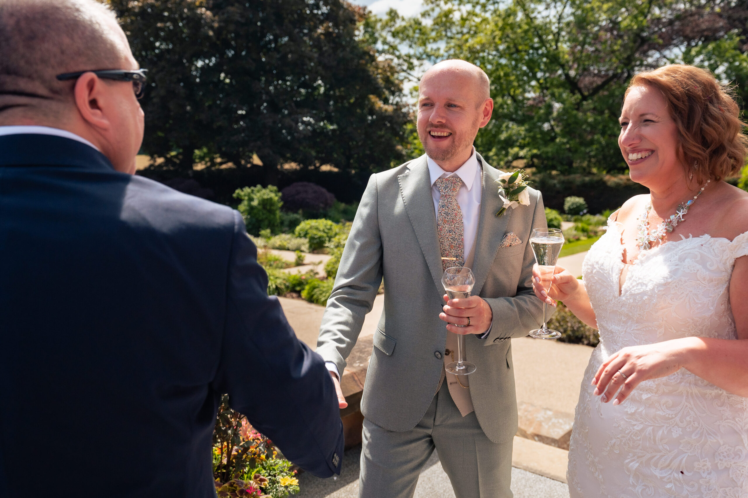Bride and groom celebrating with a glass of champagne with a guest in the Salt House gardens