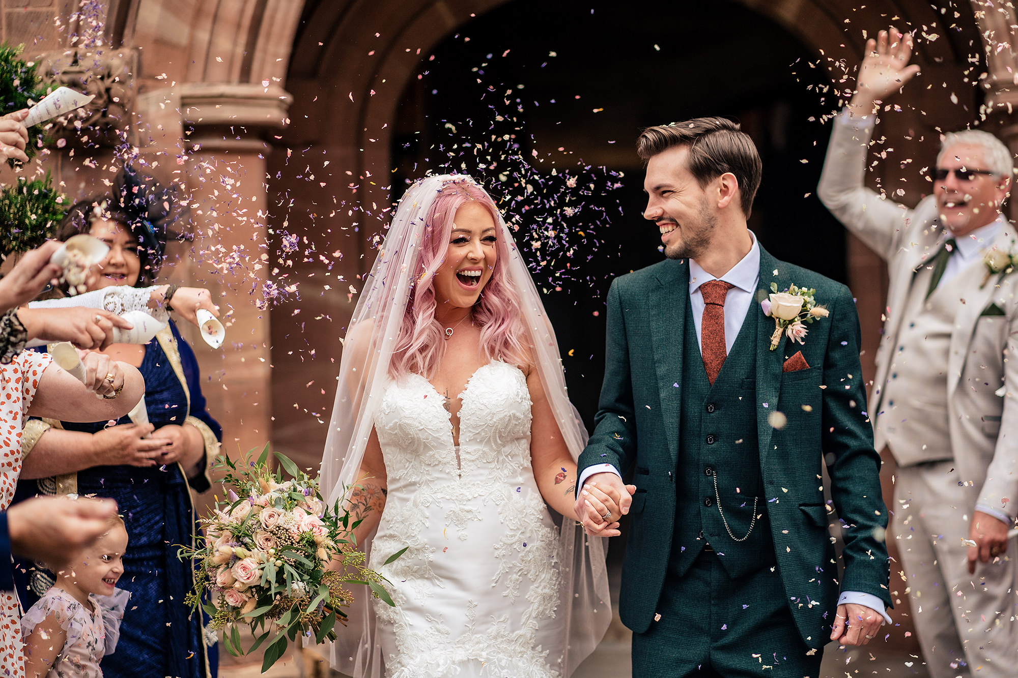 Bride and groom laughing as confetti rains down outside Standon Hall