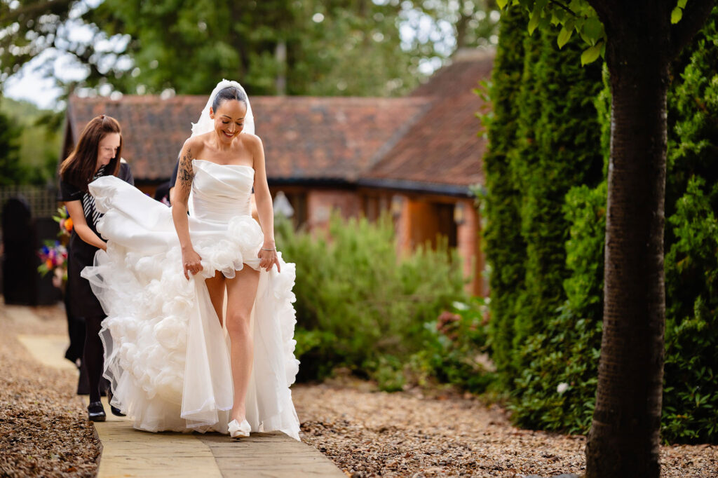 Kim lifting her skirt as she walks the path to the ceremony, her train carried behind her, Swancar Farm wedding photographer