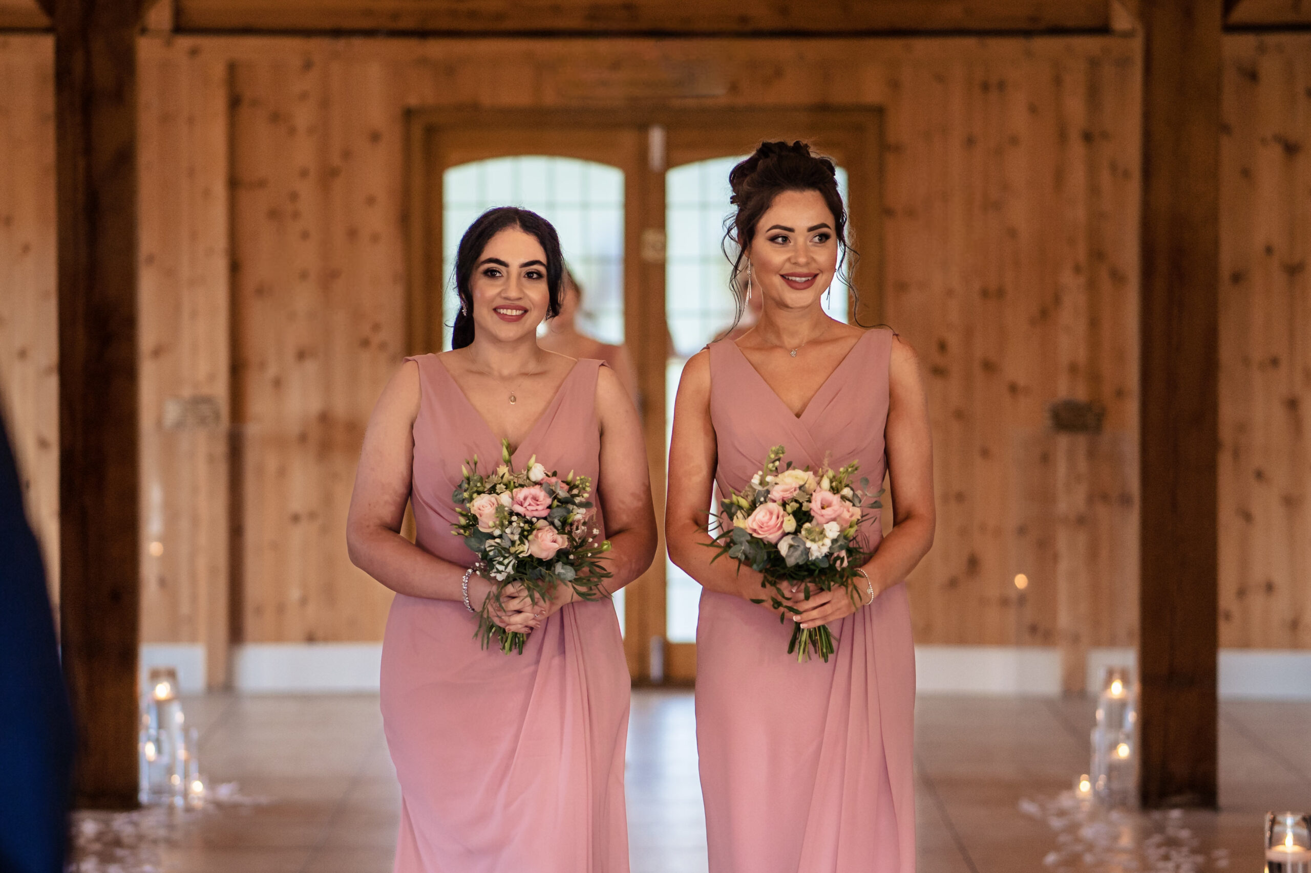 Two bridesmaids in dusky pink walking down the aisle of the Ceremony Room at Merrydale Manor