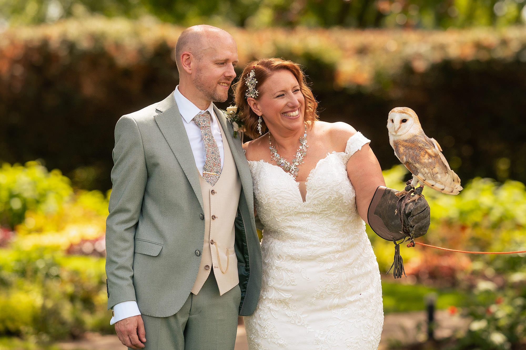 Bride and groom posing together in the gardens at Salt House with the barn owl perched between them