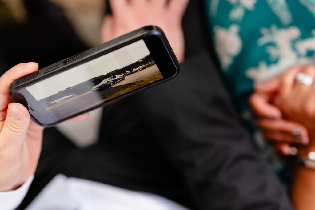 A guest's phone playing a video of a car on an airfield runway before the groom's entrance, Nottingham wedding photographer