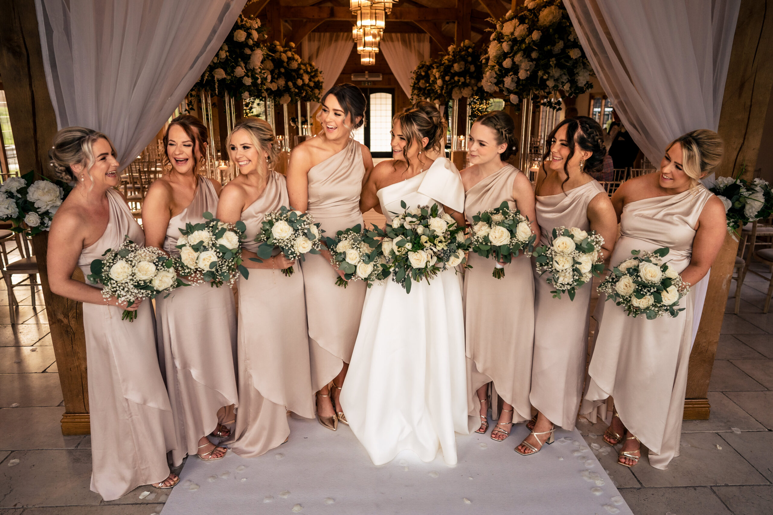 The bridesmaids together at the floral arch, champagne dresses and bouquets