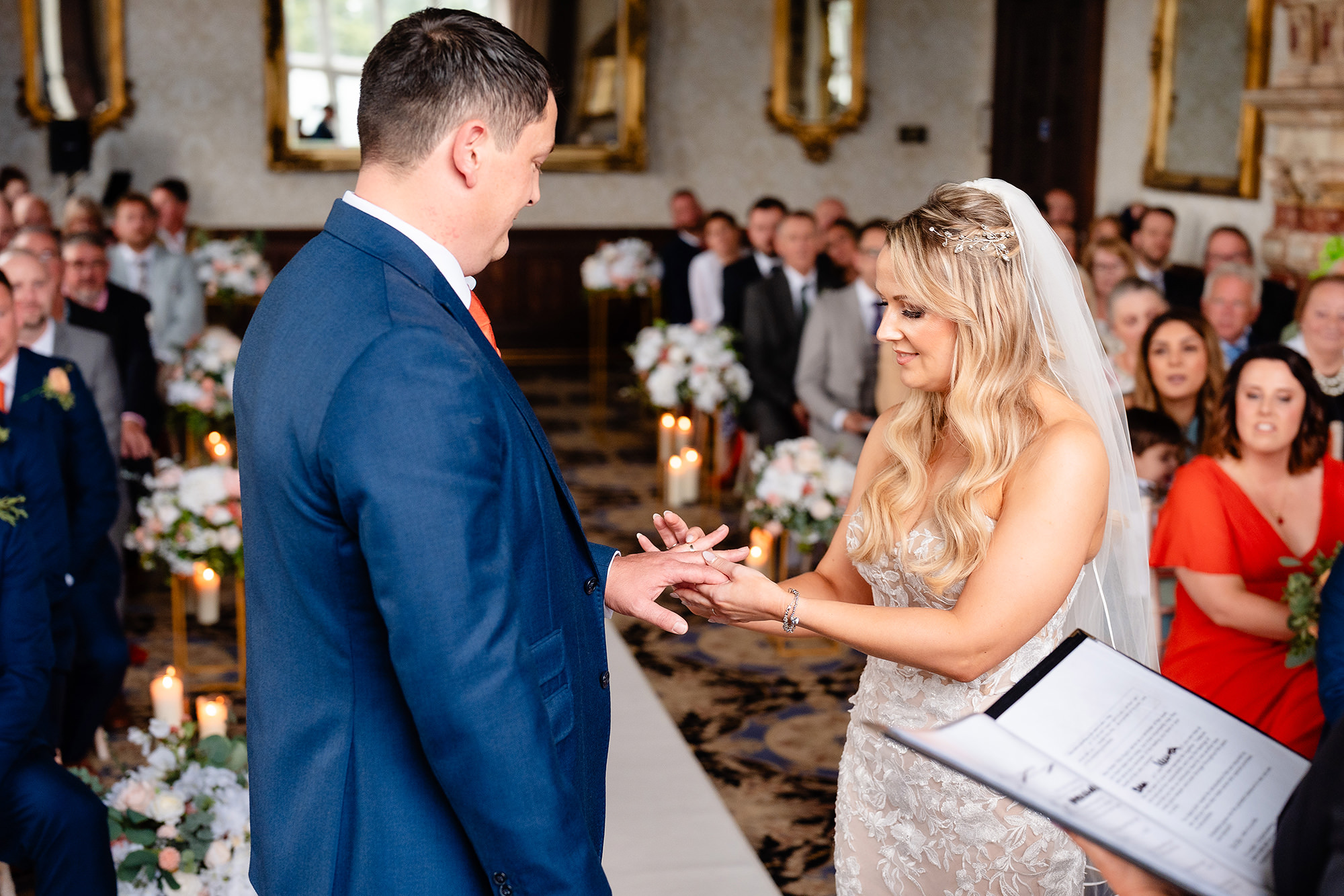 The bride sliding the ring onto the groom’s finger in front of their guests at Crewe Hall