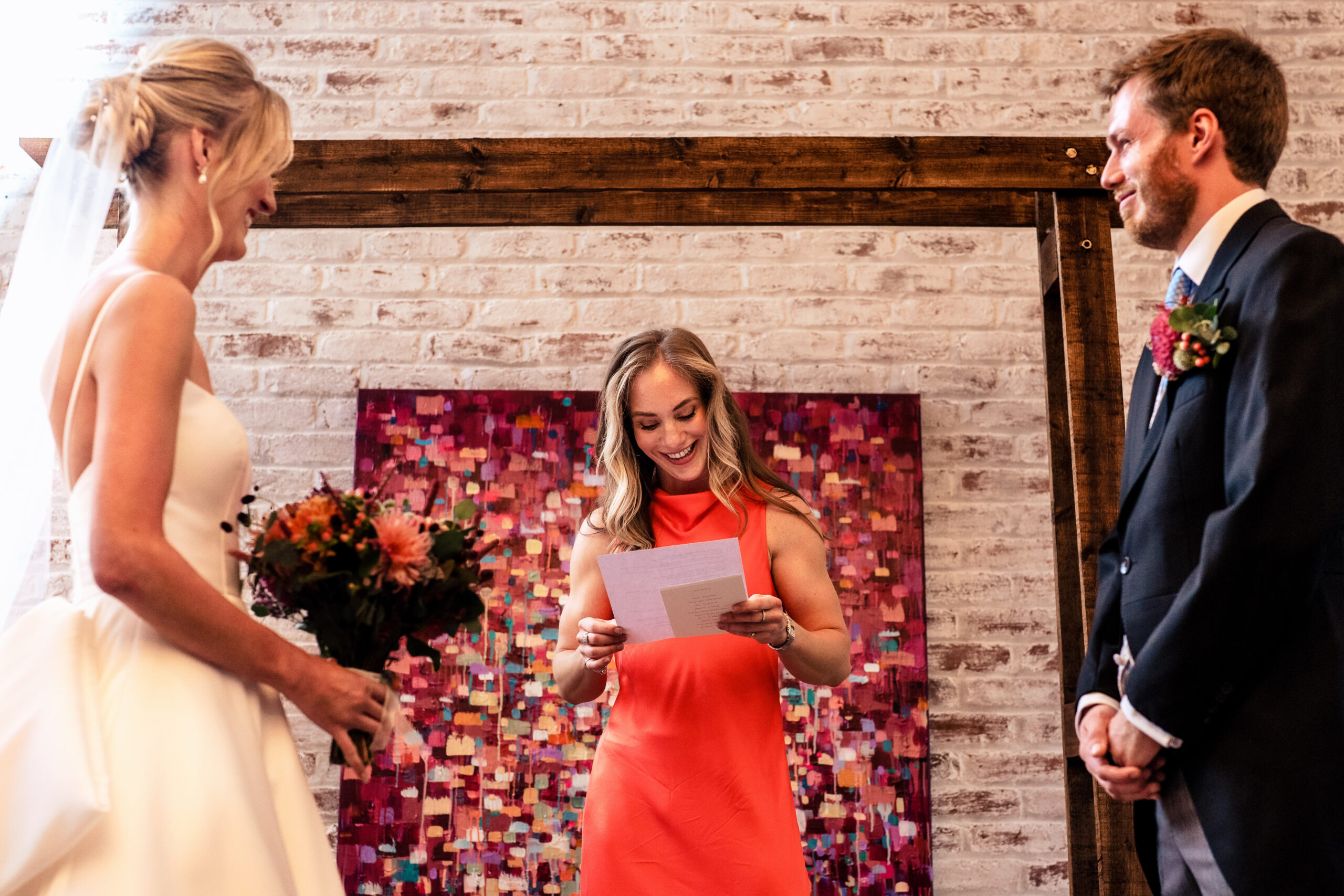 Wedding reading delivered in front of the flower wall in the Coach House at Dorfold Hall
