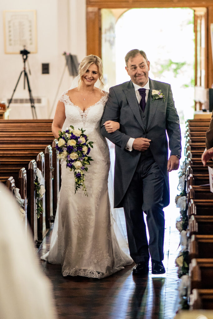 Bride walking down the aisle of St James Church Didsbury with a purple and cream cascading bouquet, Cheshire wedding photographer