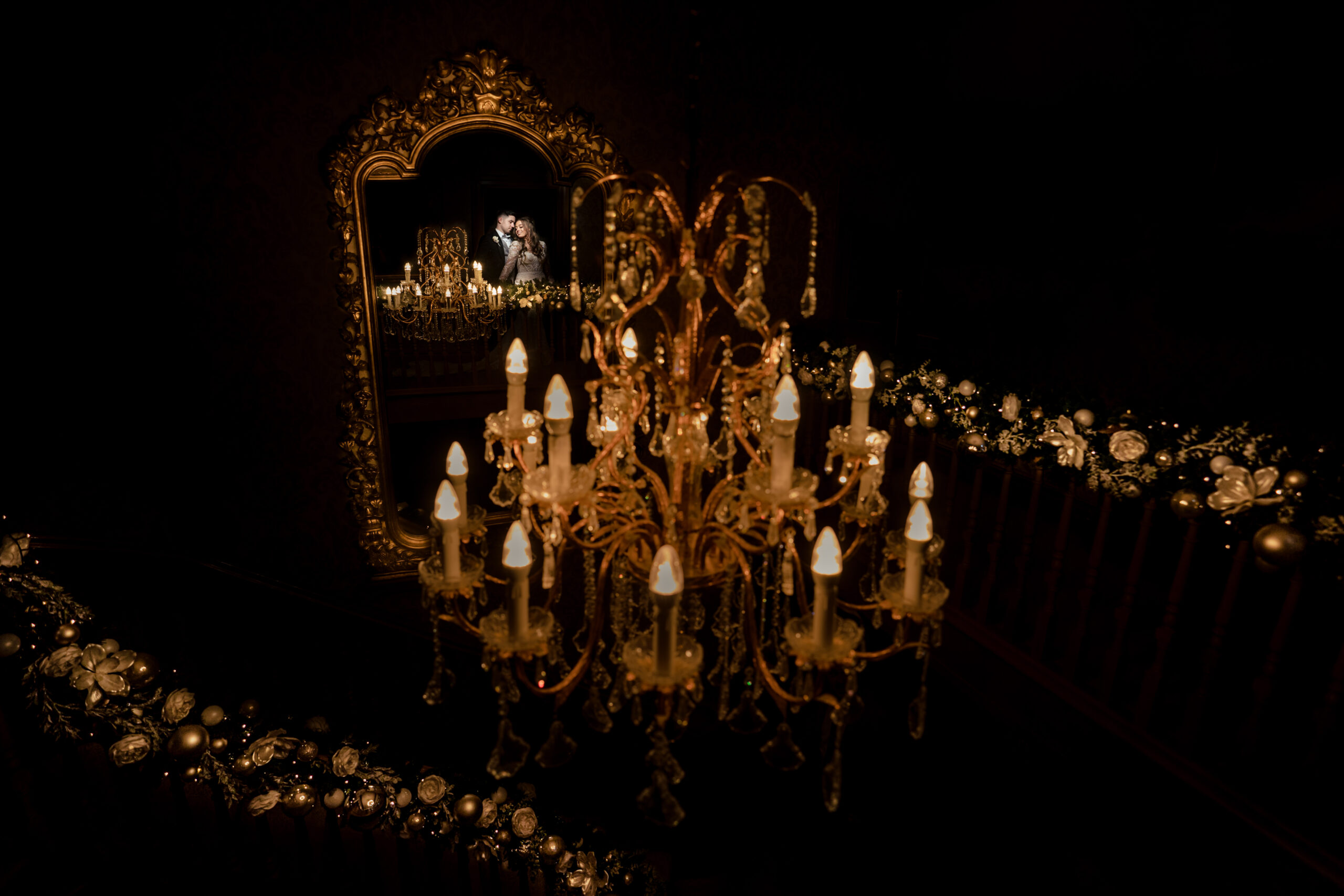 An ornate chandelier and garland reflected in a gilt mirror at night at Merrydale Manor