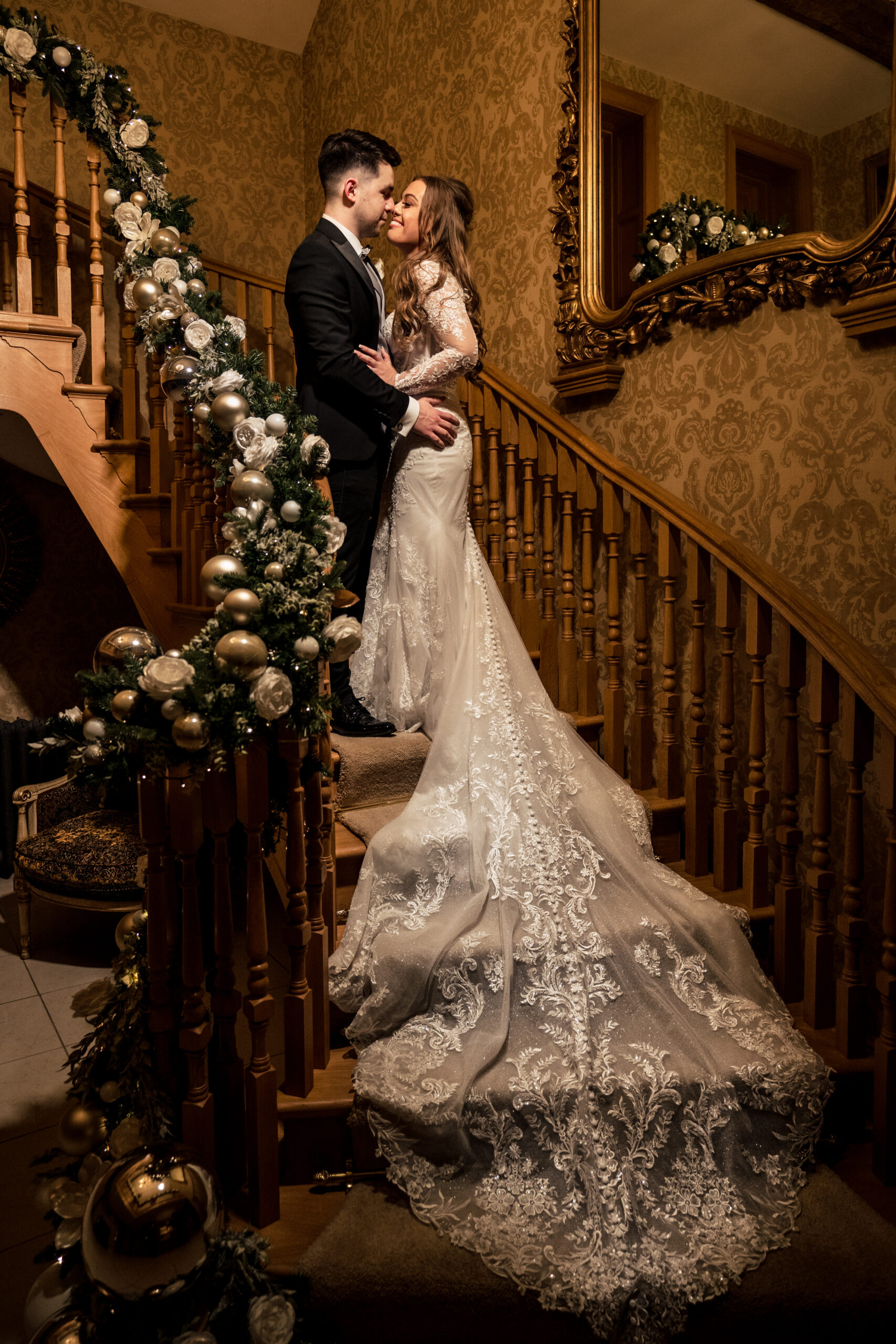 Abbie and Jamie kissing on the garland wrapped staircase with her lace train spilling down the steps, Merrydale Manor wedding photographer