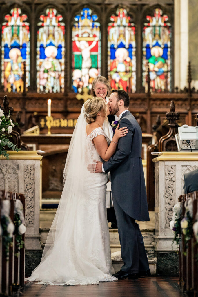 Bride and groom's first kiss at the altar beneath the stained glass window, Cheshire wedding photographer