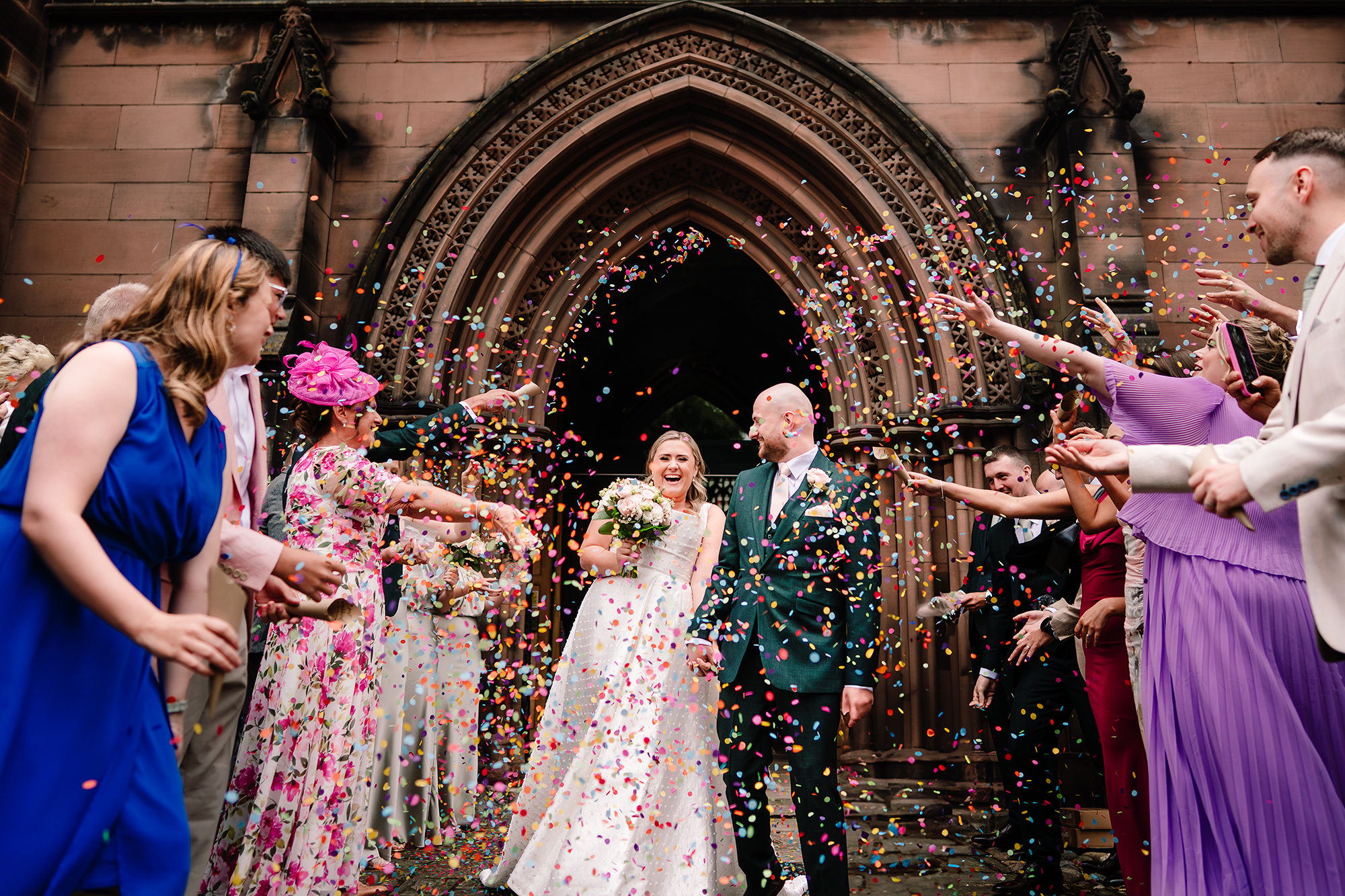 A colourful confetti explosion around Chloe and Pete and their guests outside the church