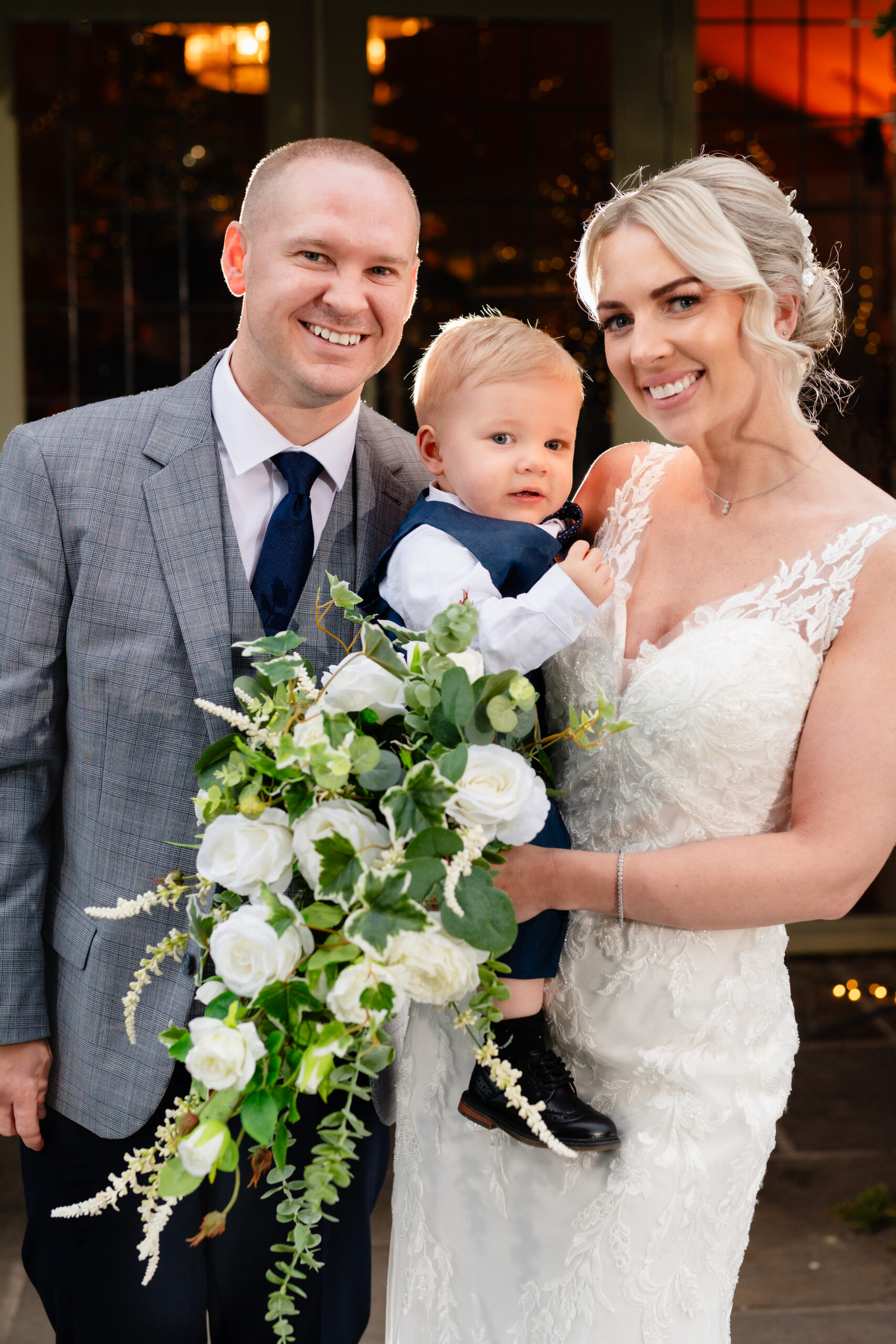 Bride and groom holding their baby son and the bridal bouquet outside the venue, Colshaw Hall winter wedding