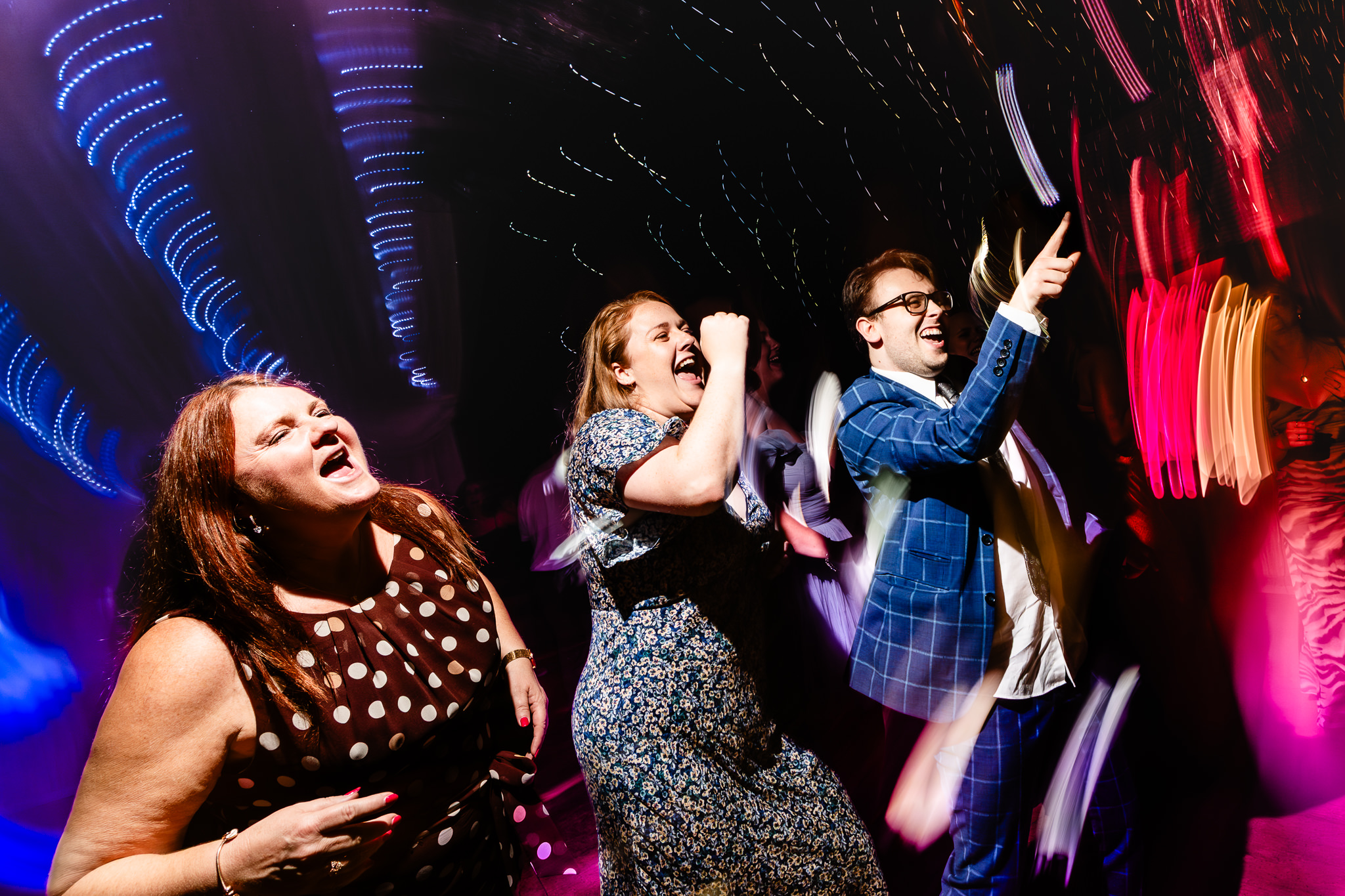 Wedding guests belting out a song on the dancefloor with light trails streaking behind them, Heaton House Farm Cheshire wedding photographer