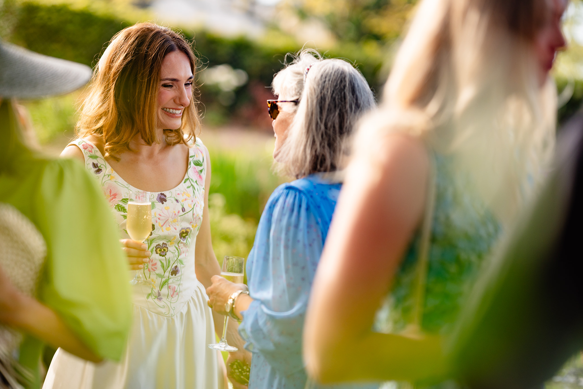Bride laughing with guests over a glass of champagne at the drinks reception