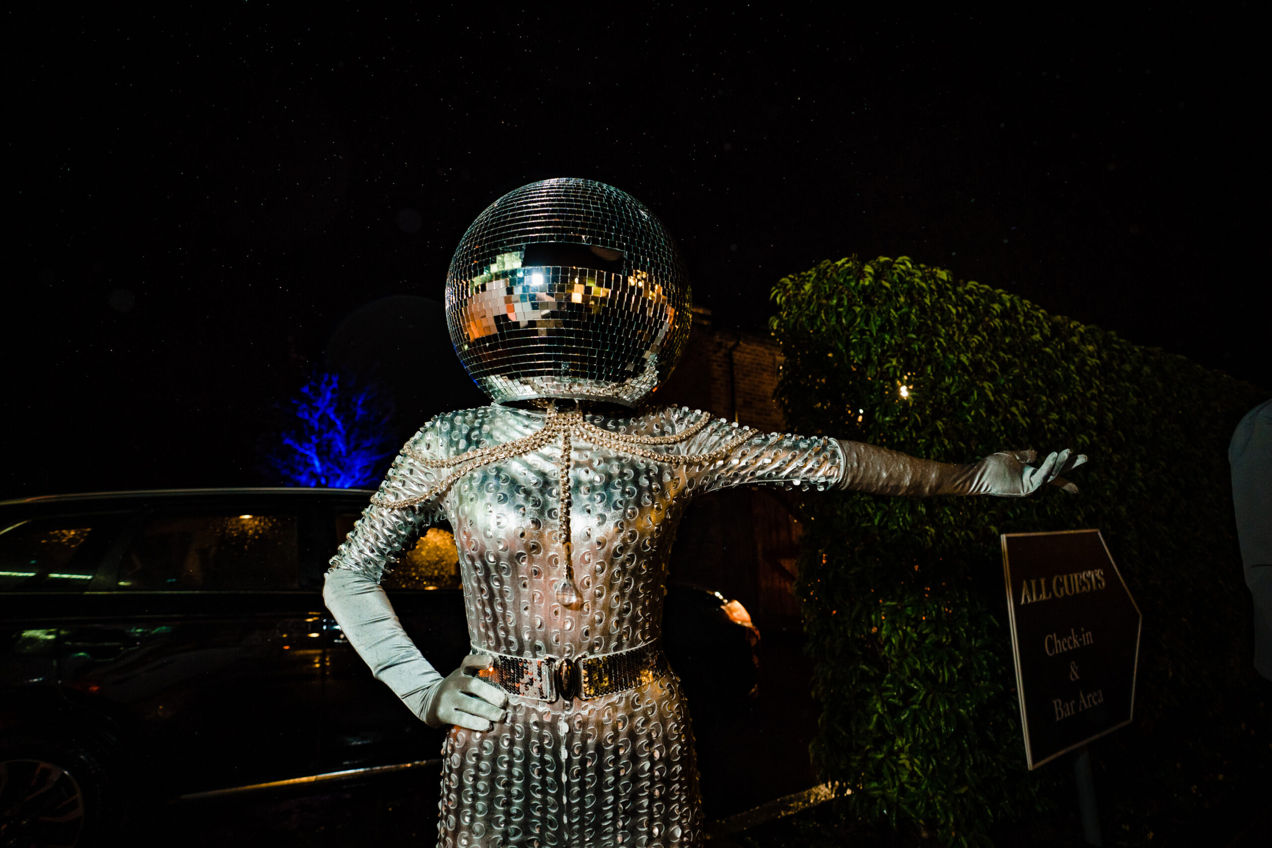 A performer in a disco ball helmet and sequinned suit posing outside at night, Cheshire wedding photographer