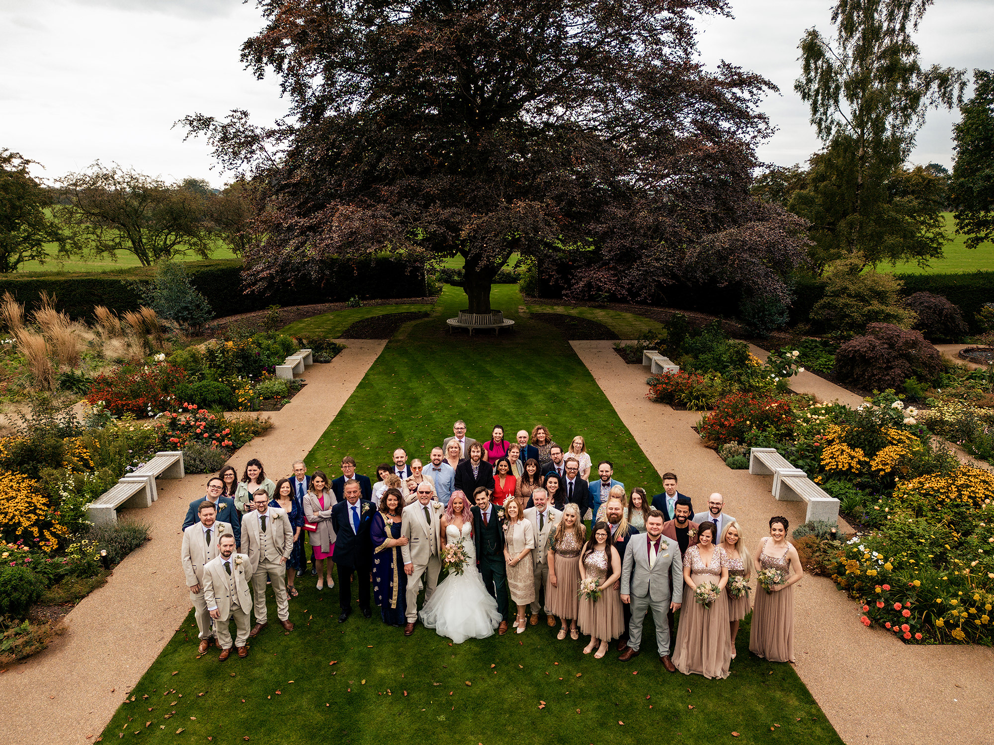 The full wedding party gathered under the tree in the garden at Standon Hall