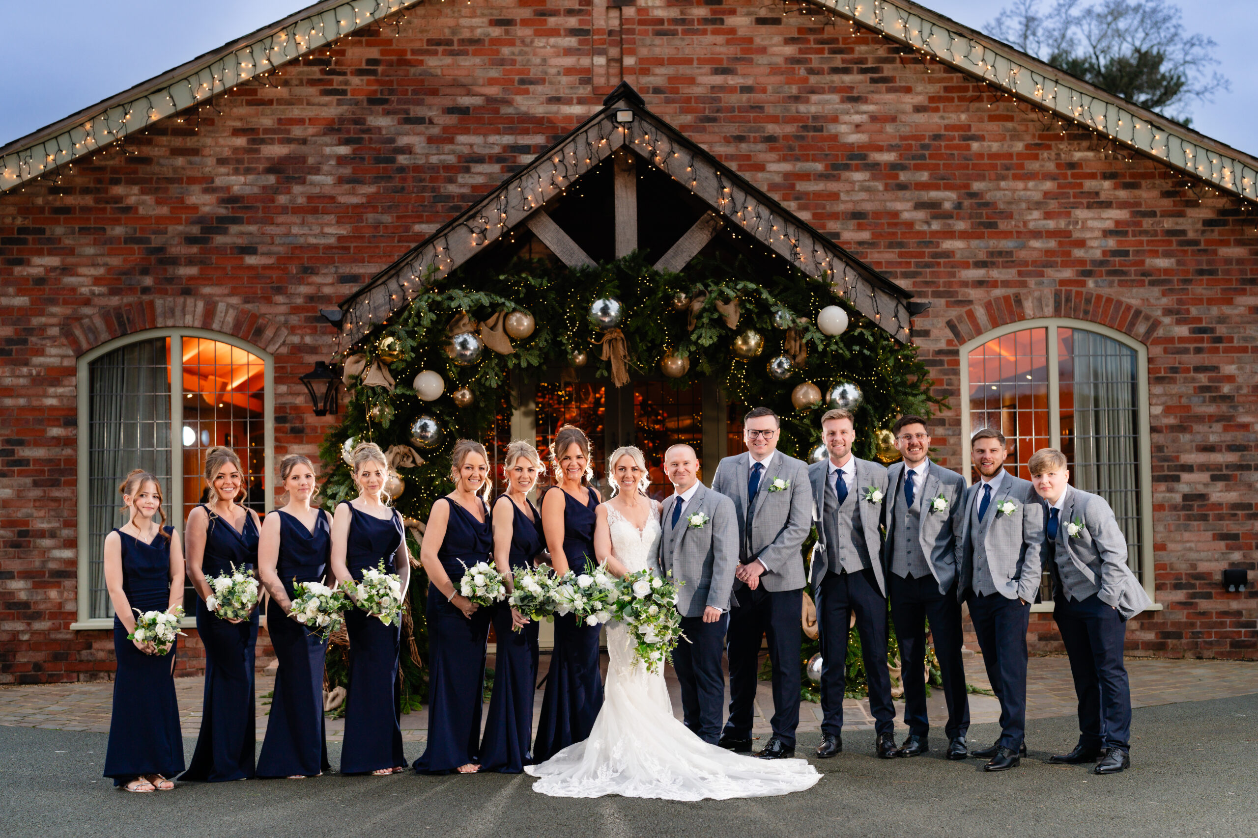 The full bridal party lined up under the Christmas garland arch outside Colshaw Hall, Cheshire wedding photographer