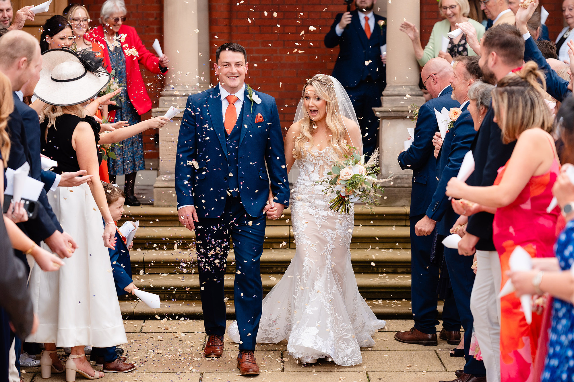 Bride and groom walking down the back steps of Crewe Hall through a shower of confetti thrown by their guests