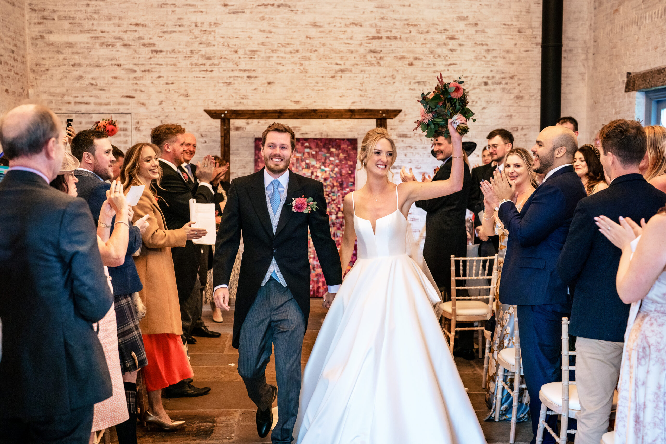 Bride punching the air as the couple walk back up the aisle to cheering guests at Dorfold Hall
