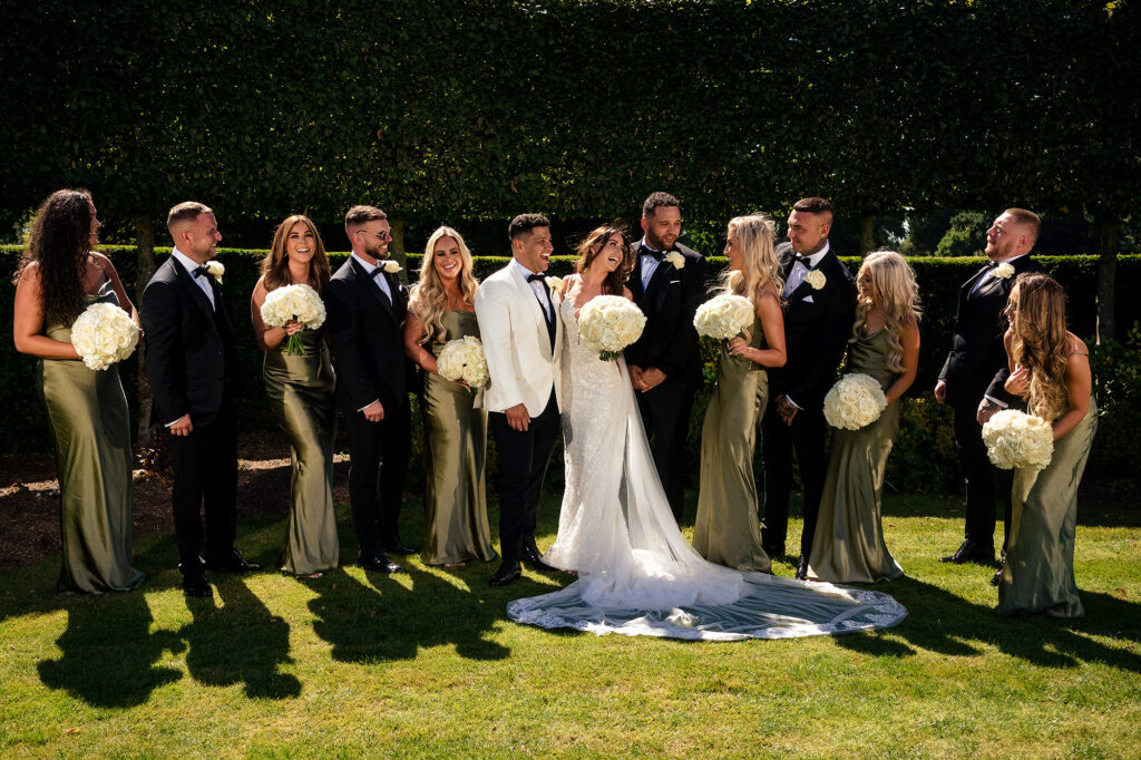 Gemma and Tyrone laughing with their bridesmaids in olive satin and groomsmen on the lawn at Merrydale Manor, Cheshire wedding photographer