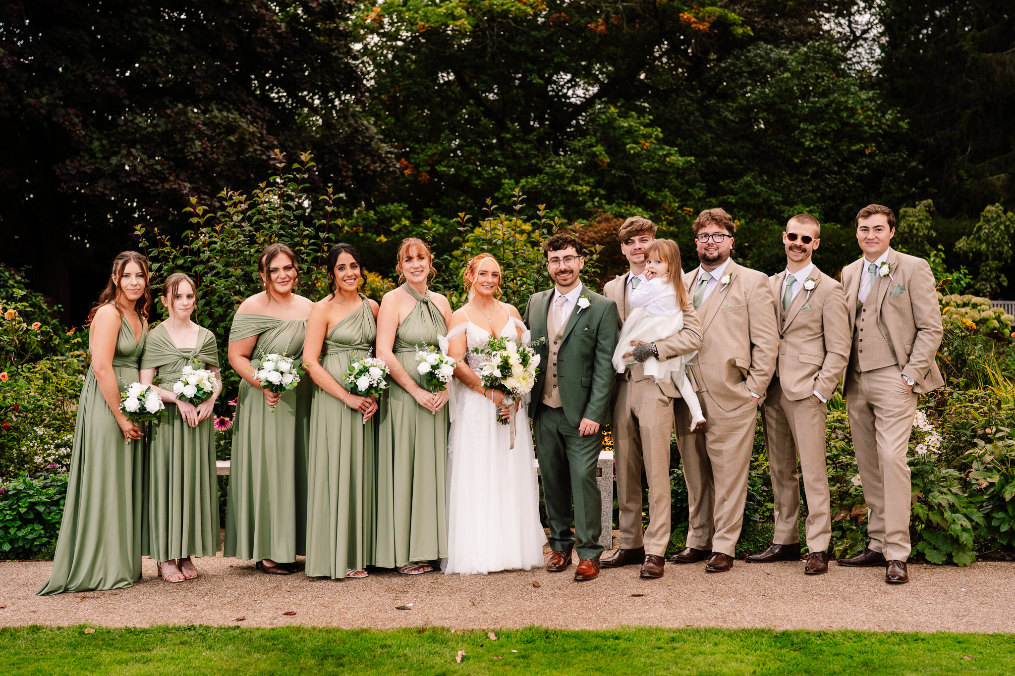 The full bridal party posing together in the gardens at Salt House, bridesmaids in sage green