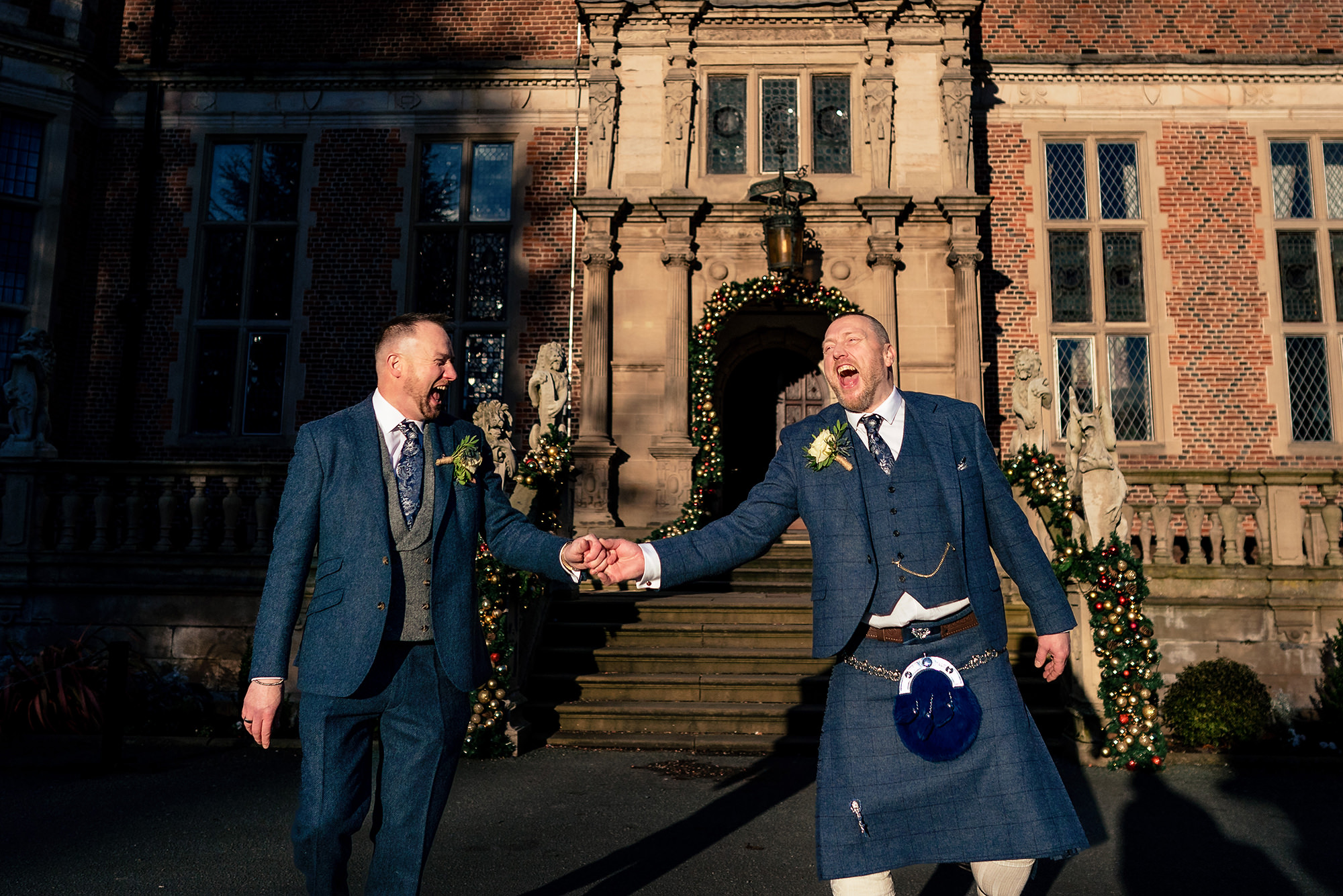 John and Neill laughing and clasping hands together in front of Crewe Hall, just the two of them for a moment