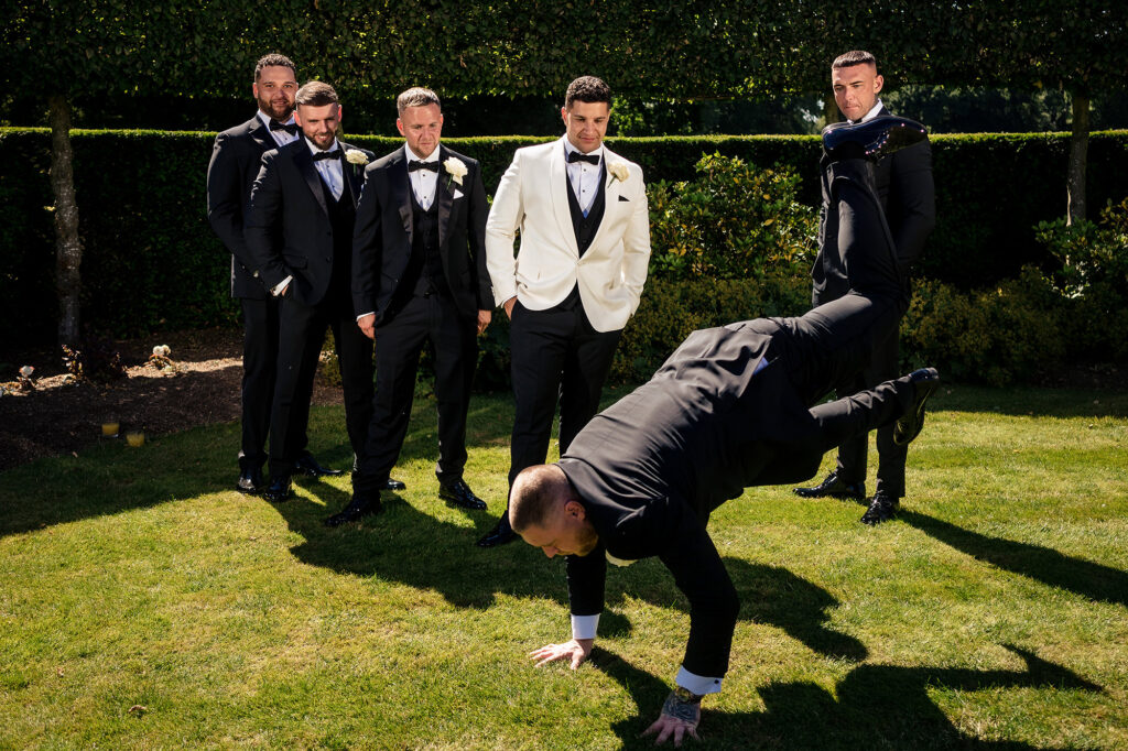 A groomsman doing a handstand on the lawn while Tyrone and the other groomsmen watch