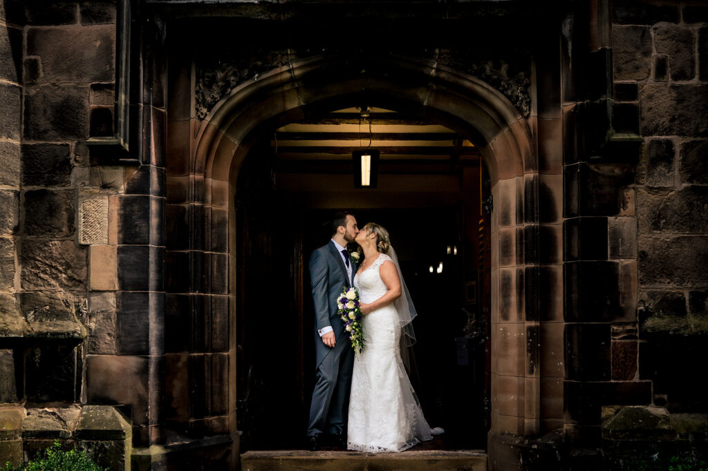Bride and groom kissing in the stone doorway of St James Church, Merrydale Manor wedding photographer