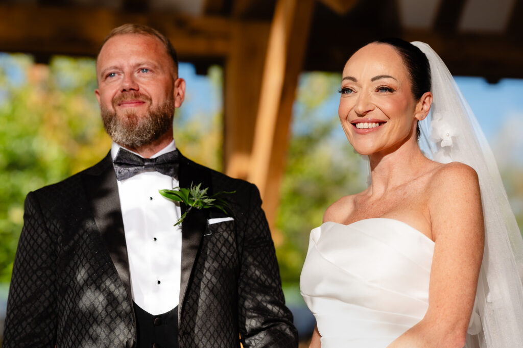 Kim and Glynn smiling side by side in dappled sunlight at the front of the ceremony, Swancar Farm wedding photographer