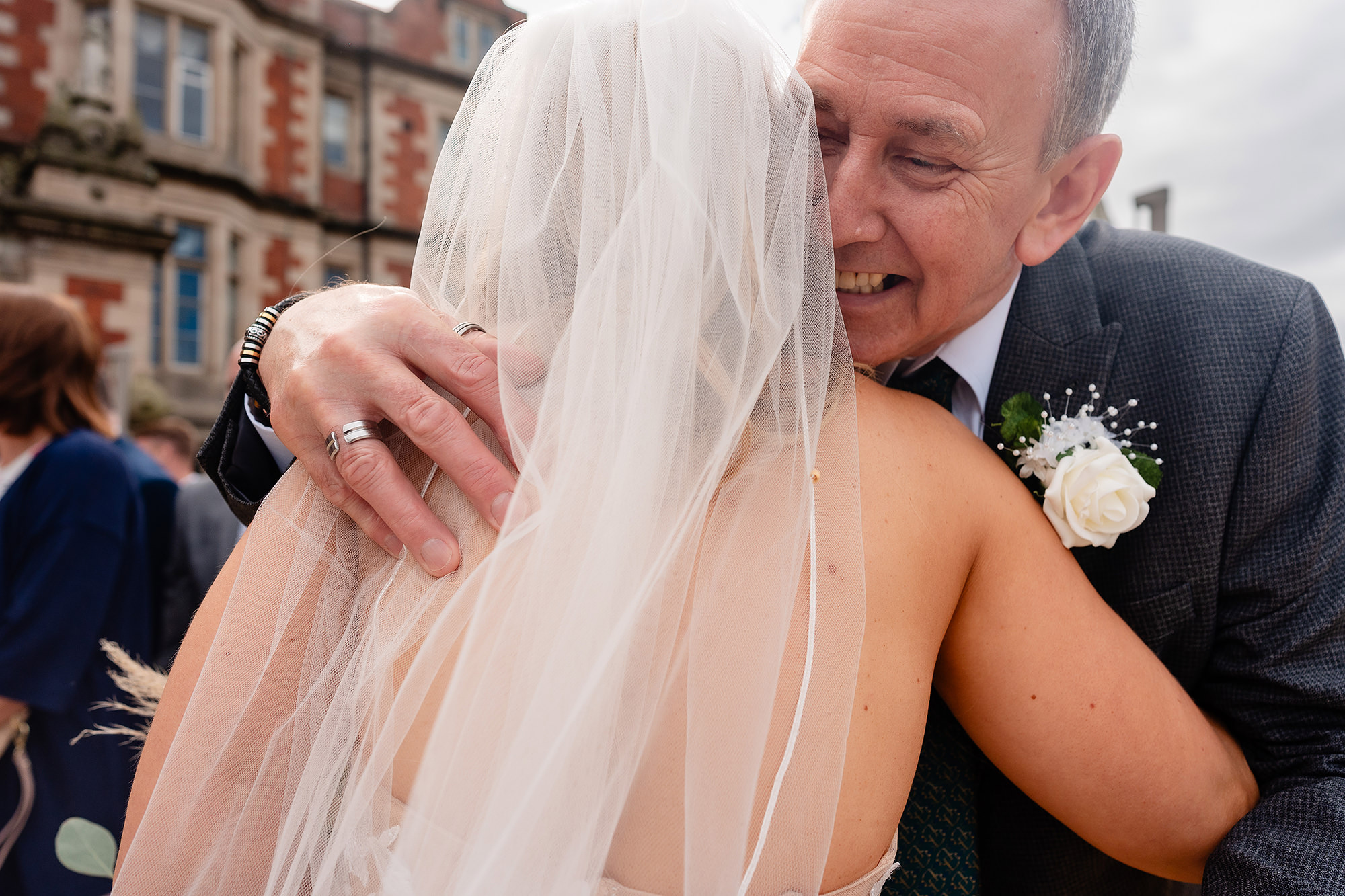 The bride in her veil hugging an older man in a grey suit outside Crewe Hall