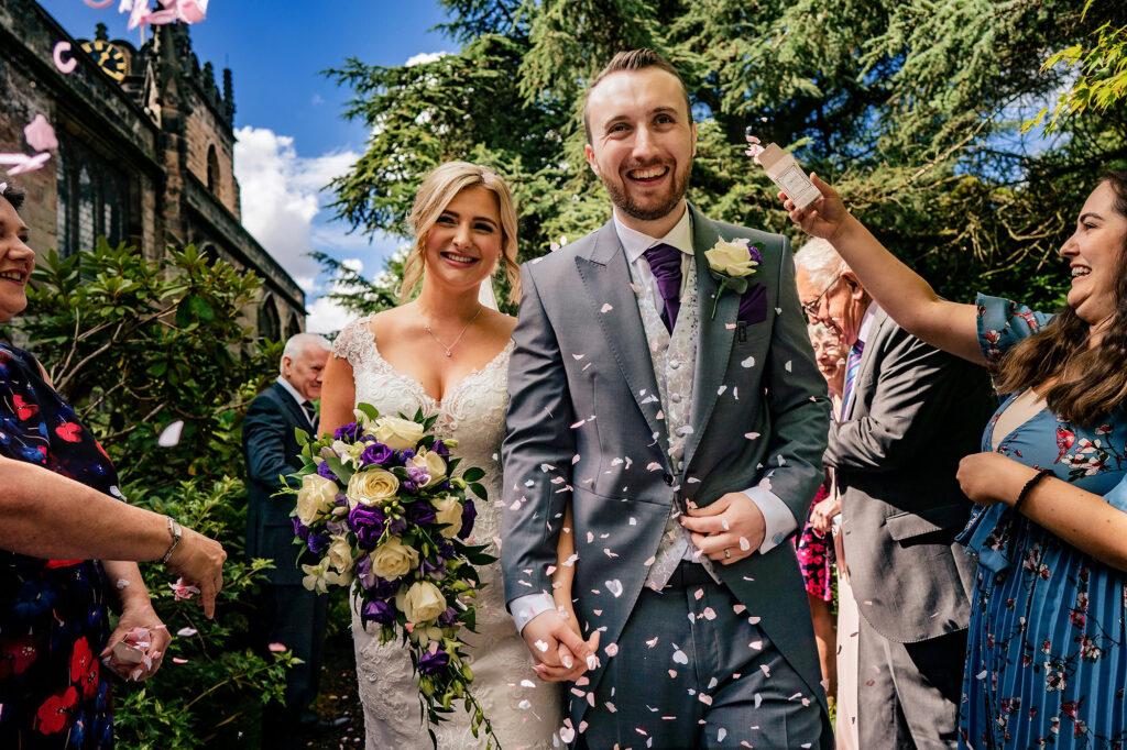 Bride and groom laughing through a shower of confetti outside the church, Cheshire wedding photographer