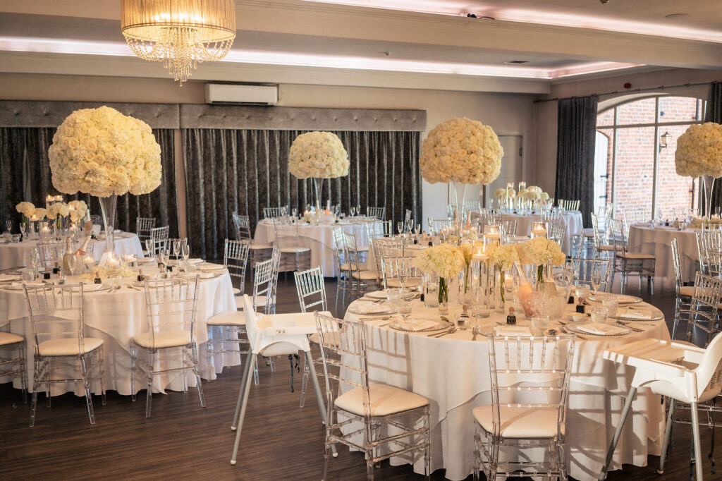The wedding breakfast room at Merrydale Manor set with tall white rose centrepieces and clear chairs