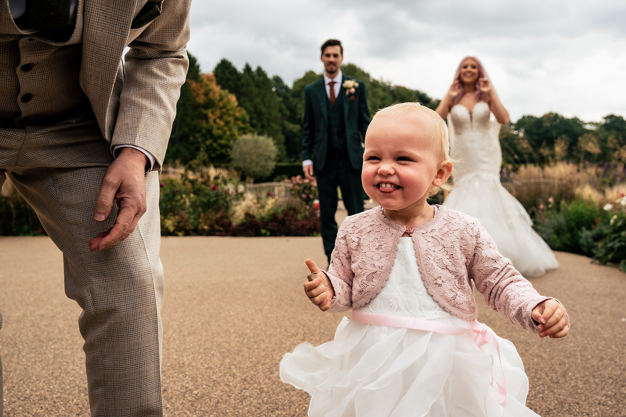 The couple’s little girl running towards the camera with the newlyweds behind her at Standon Hall