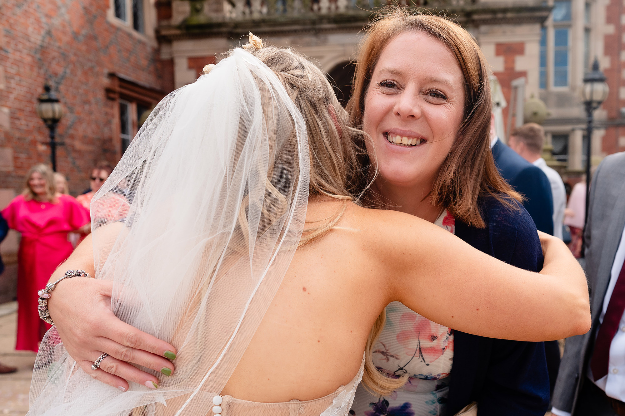 A guest hugging the bride tightly and beaming over her shoulder at the camera