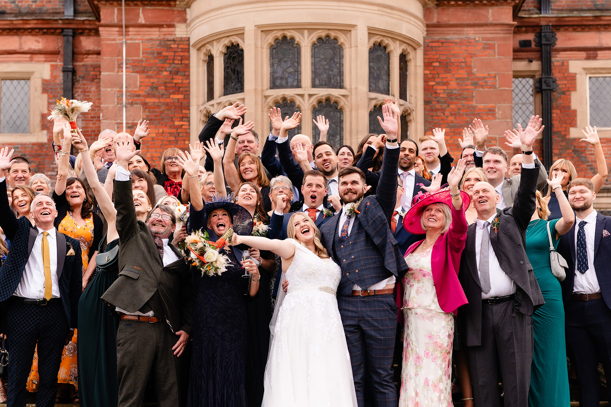 The full group of wedding guests cheering for the camera at Crewe Hall, Cheshire wedding photographer
