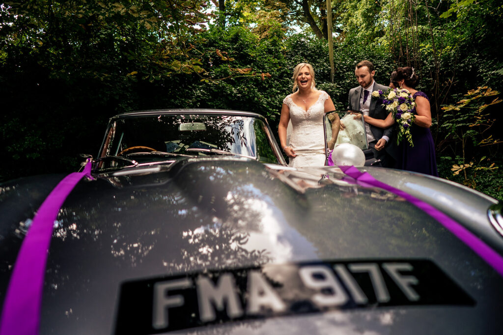 Bride and groom walking towards the E-type Jaguar with its FMA 917F plate outside the church, Merrydale Manor wedding photographer