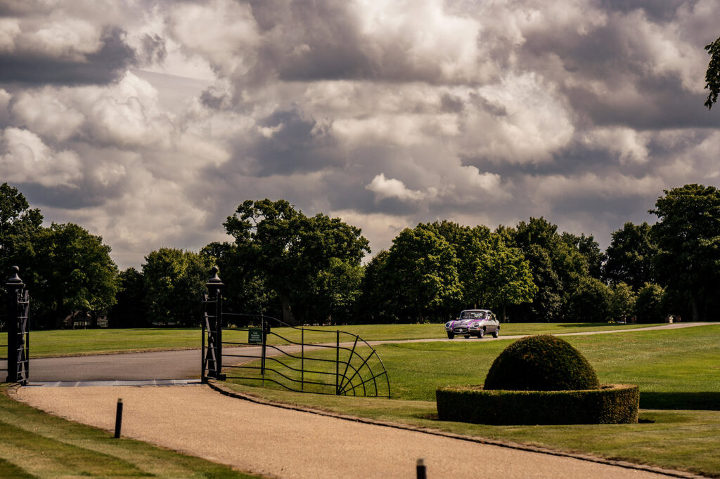 The E-type Jaguar arriving through the gates at Merrydale Manor under big summer clouds, Merrydale Manor wedding photographer