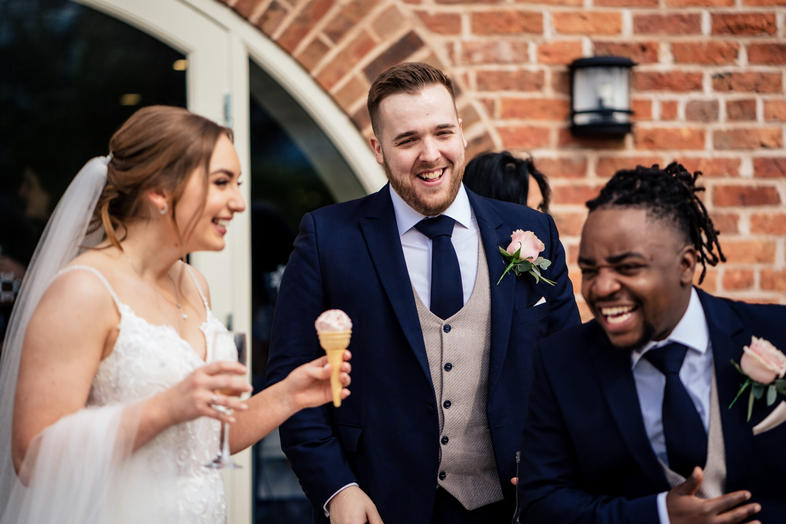 Bethany with an ice cream and a glass of fizz, laughing with two groomsmen