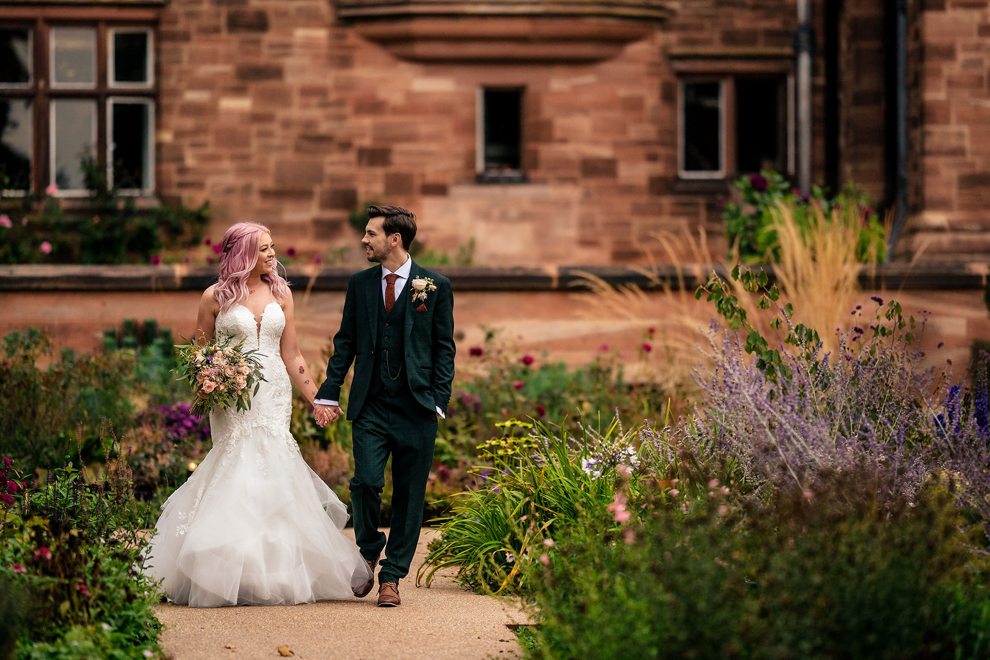 Bride and groom walking hand in hand through the gardens at Standon Hall