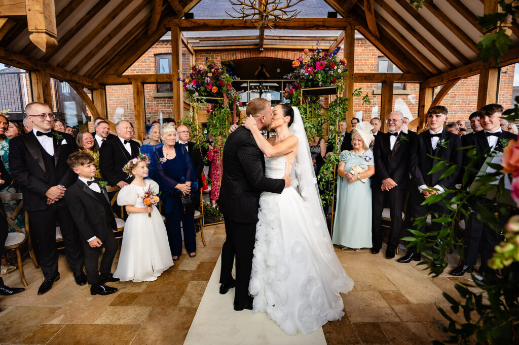 Kim and Glynn's first kiss as guests stand either side of the aisle, Swancar Farm wedding photographer