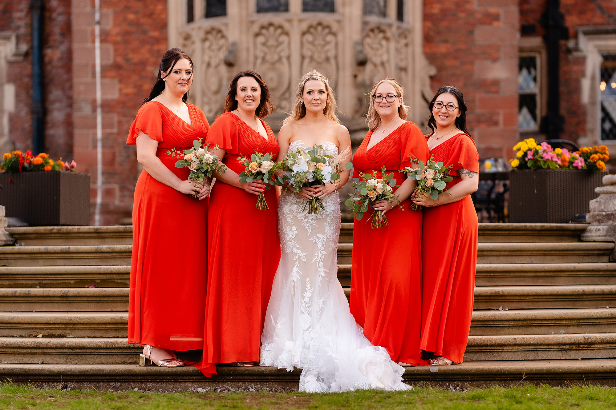 The bride with four bridesmaids in long burnt orange dresses at the back of Crewe Hall, bouquets held low