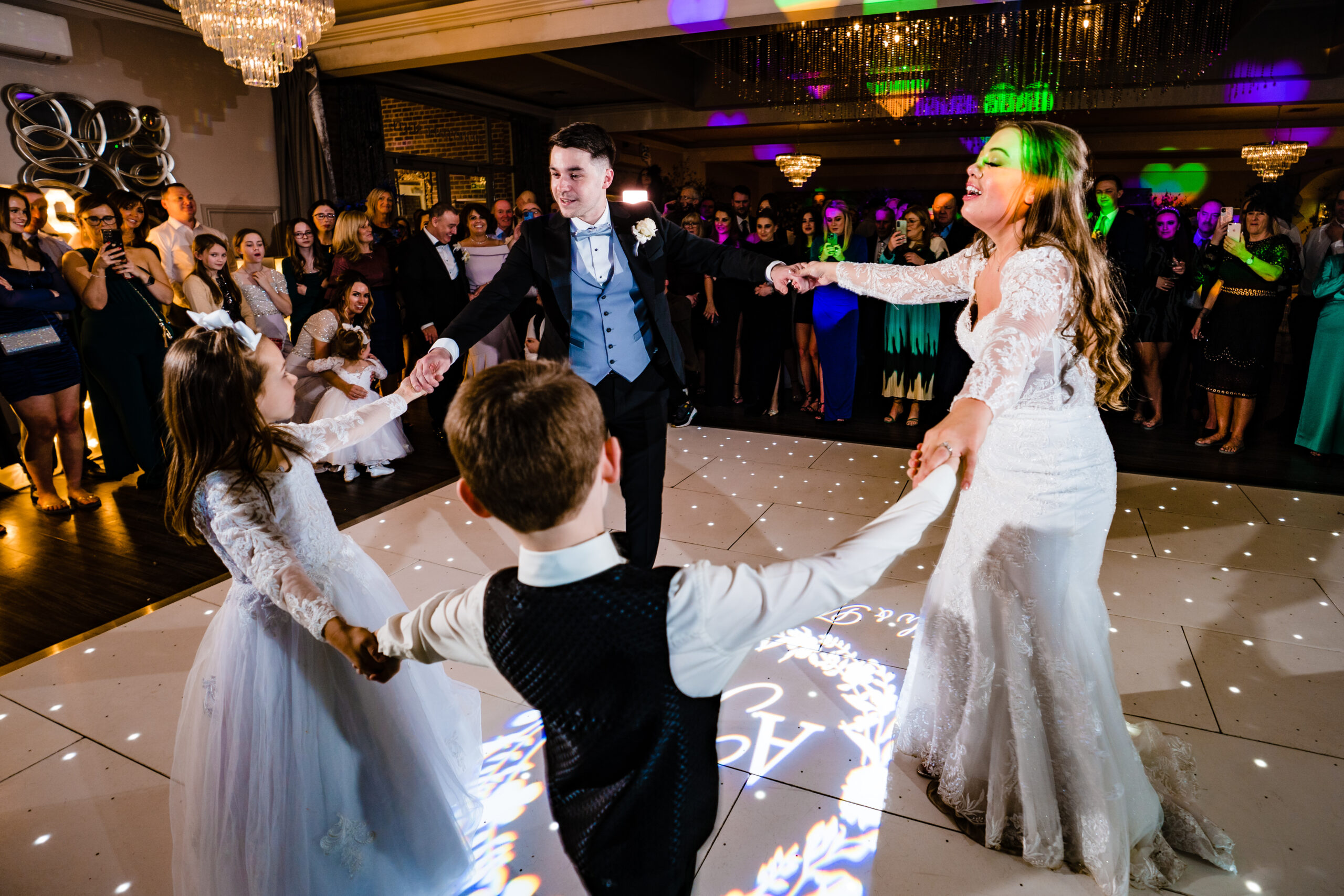 Abbie and Jamie holding hands in a circle with a little girl and boy on the dance floor, Cheshire wedding photographer