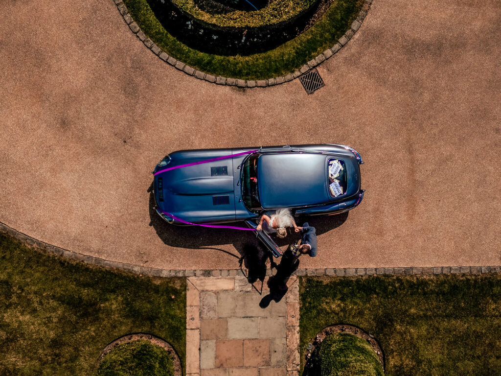 Aerial drone shot looking down on the bride, groom and E-type Jaguar on the Merrydale Manor driveway, Cheshire wedding photographer