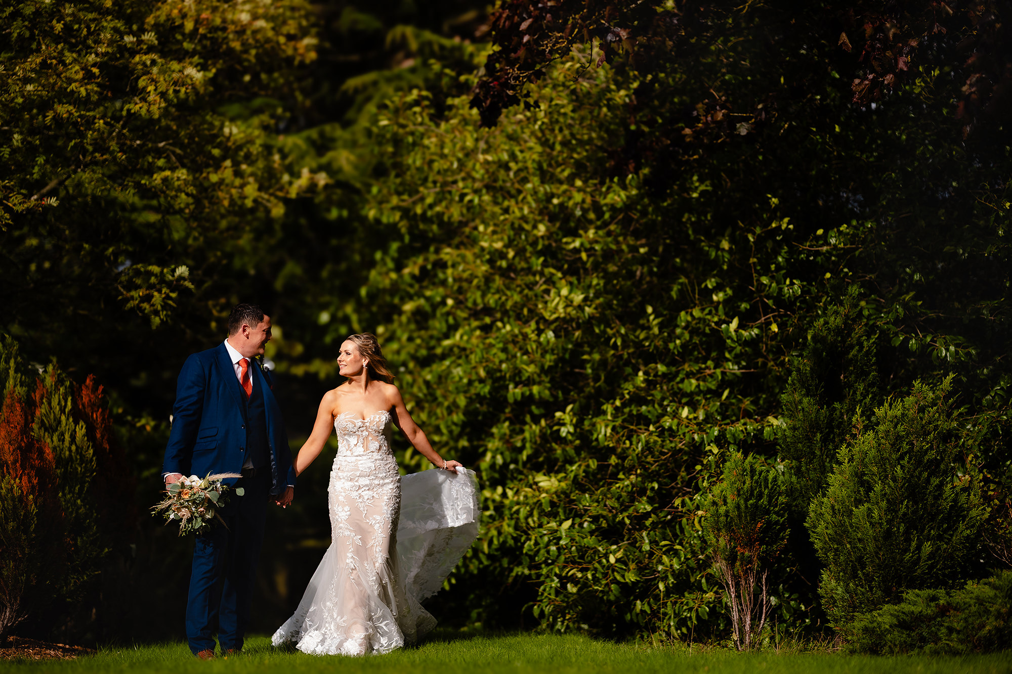 Bride and groom walking together past dark green planting in the grounds at Crewe Hall
