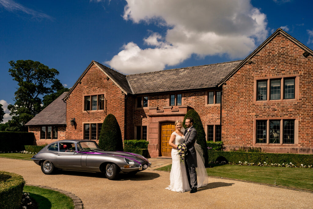 Bride and groom beside the E-type Jaguar in front of the red brick house at Merrydale Manor, Merrydale Manor wedding photographer