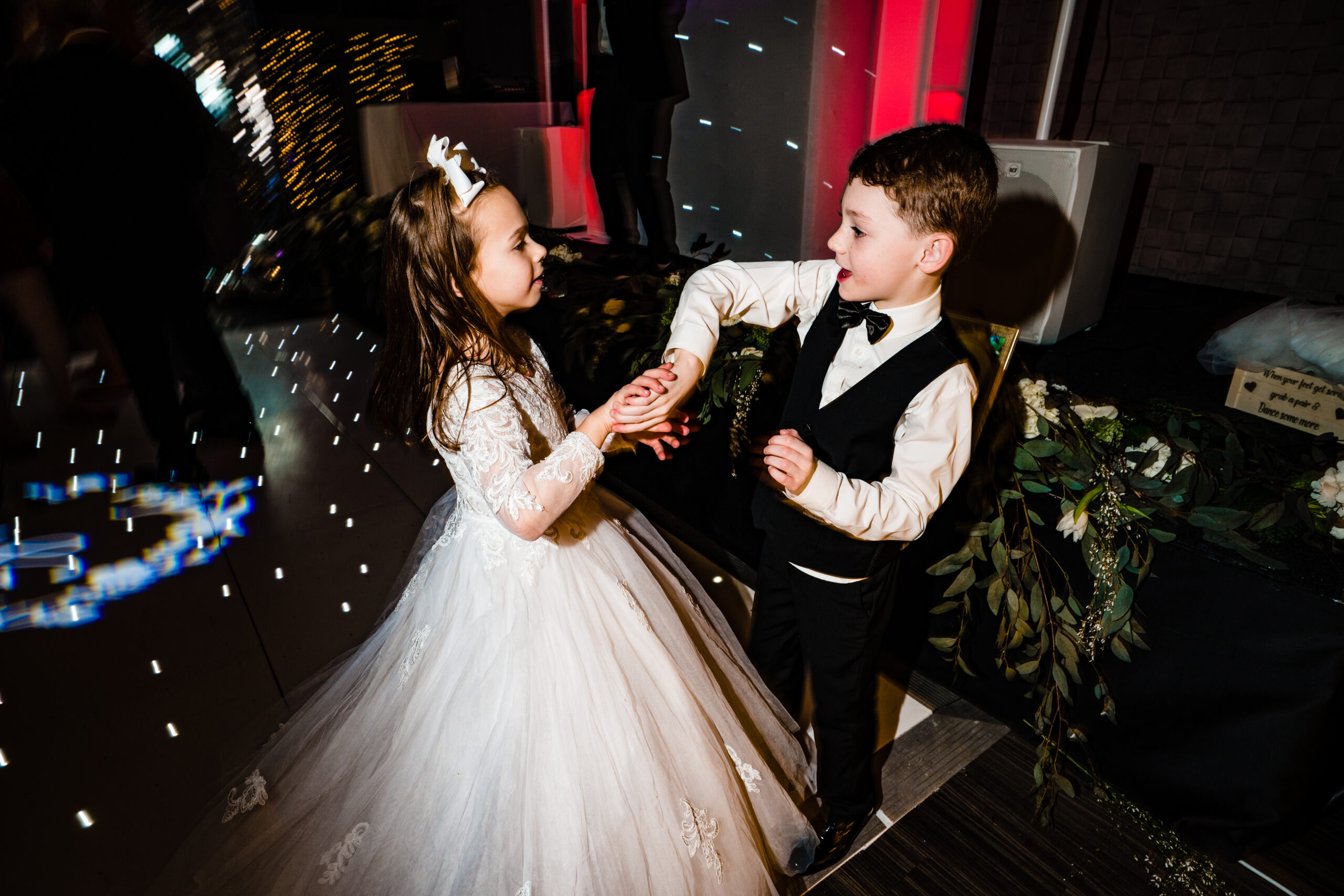A little girl in a white dress and a boy in a waistcoat dancing hand in hand at Merrydale Manor