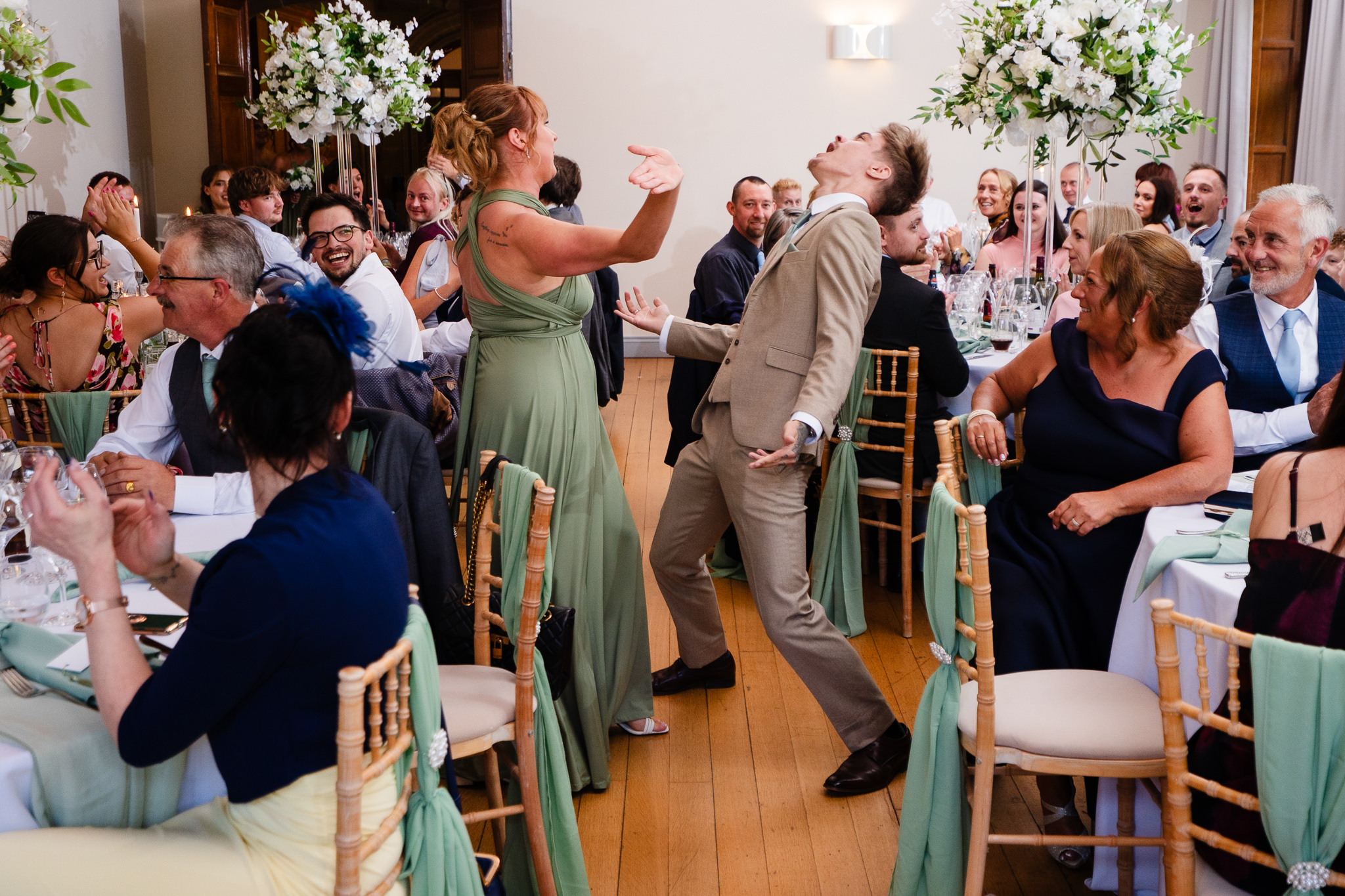 A bridesmaid and groomsman dancing into the reception room as guests clap and cheer