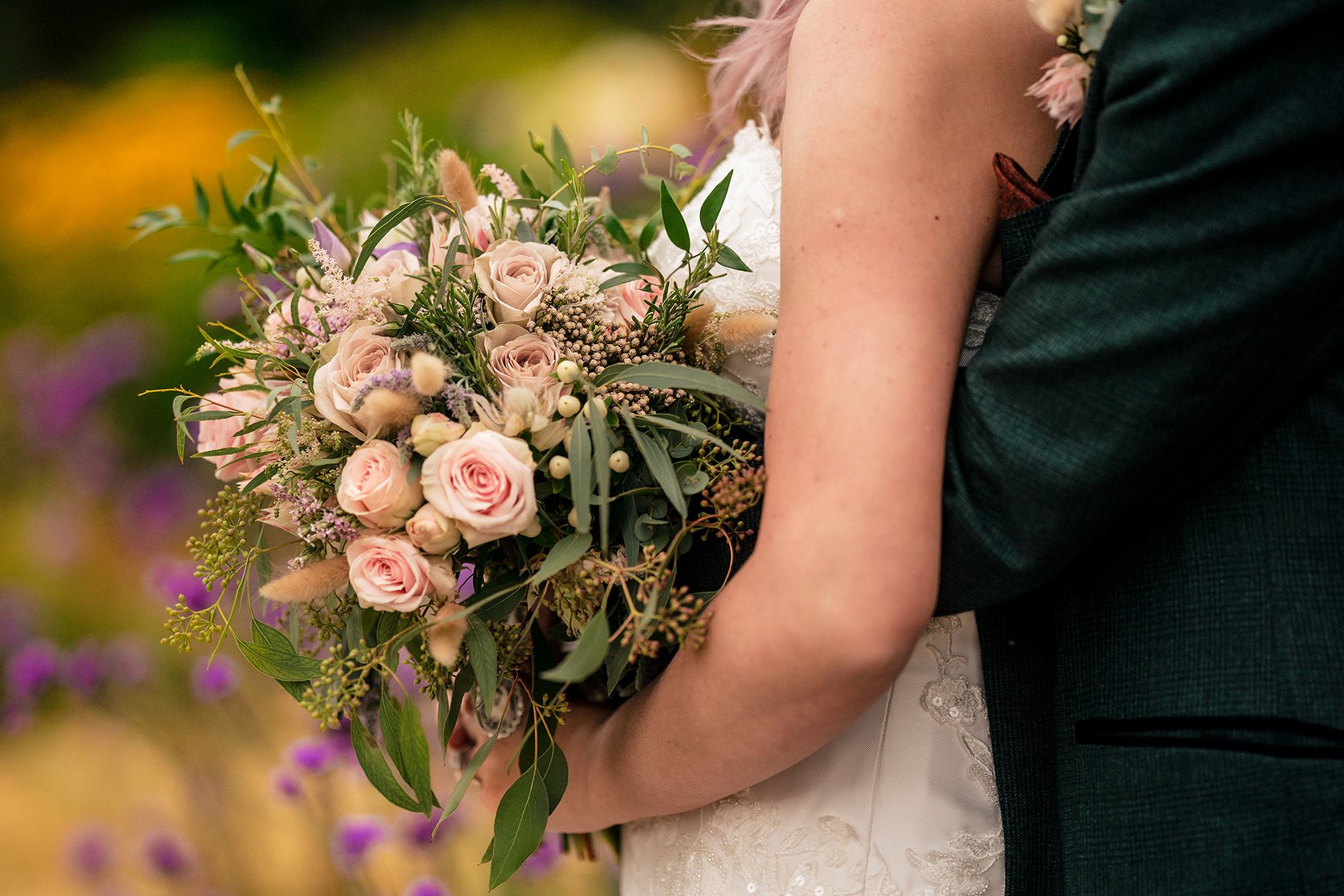 Close up of the bride’s bouquet as the groom holds her close at Standon Hall