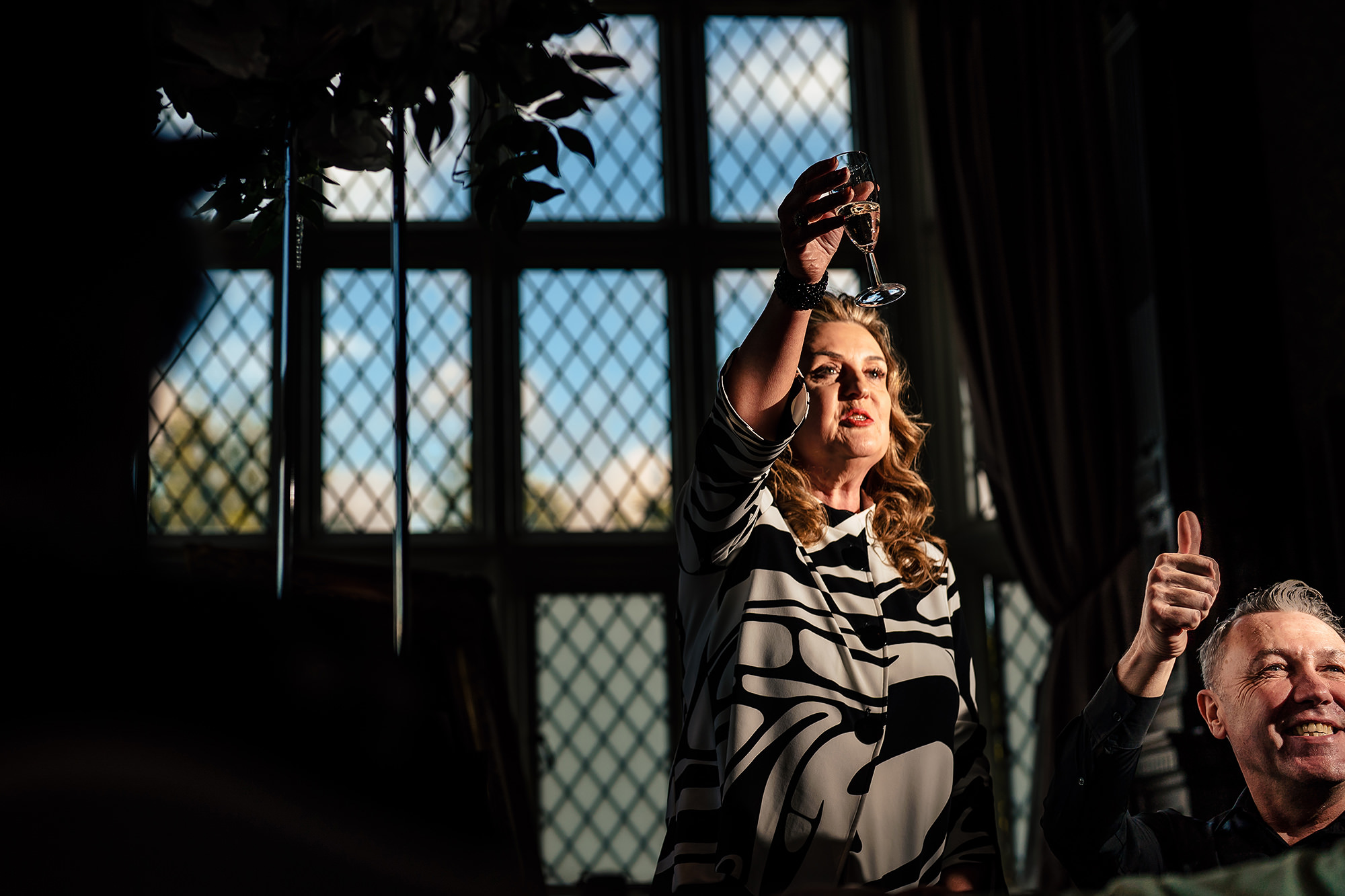 A guest raising a glass by the window during the speeches at Crewe Hall